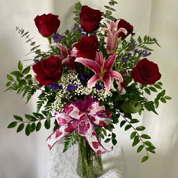 Red roses and pink lilies in a glass vase with a ribbon bow
