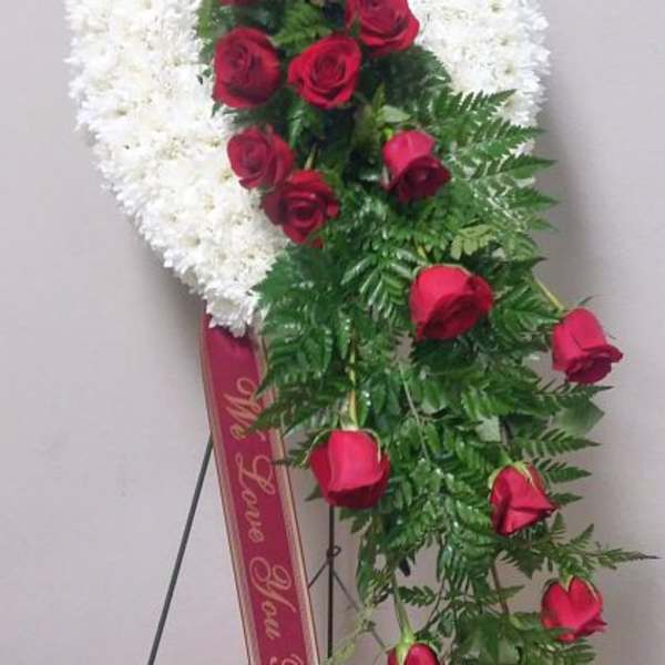 Standing floral wreath with white flowers and red roses on a ribboned easel