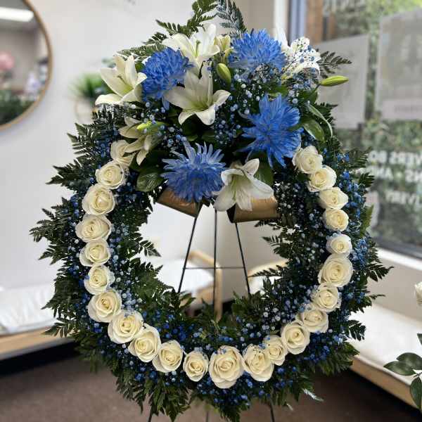 Large floral wreath with white roses, lilies, and blue flowers on a stand