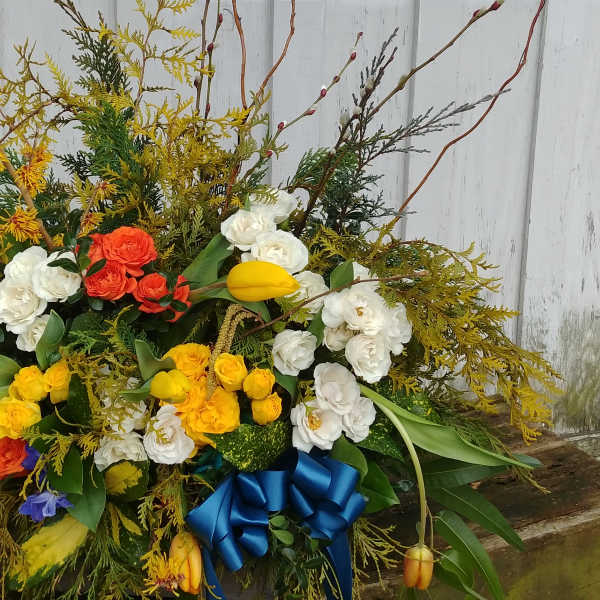Large mixed floral arrangement with white, yellow, and orange blooms and a blue ribbon