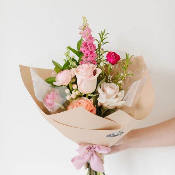 Hand-tied bouquet of pink and white roses wrapped in beige paper