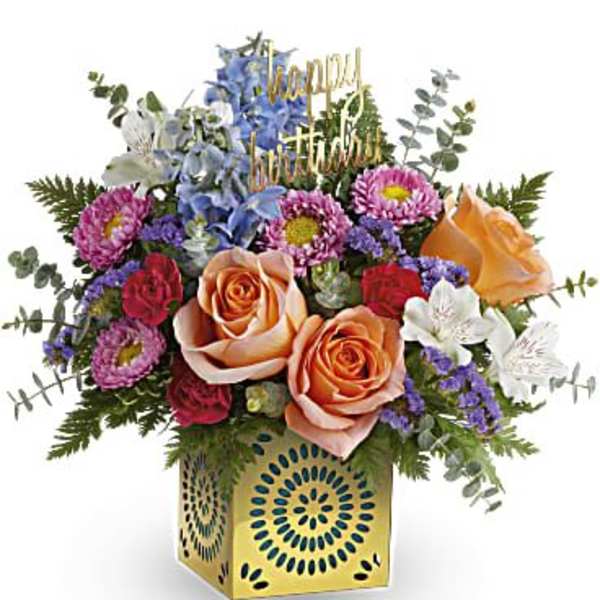 Colorful birthday flower arrangement with peach roses in a yellow cube vase and happy birthday pick