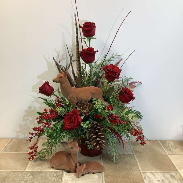 Red roses in a holiday arrangement with deer figurines and pinecones