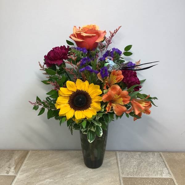 Mixed bouquet with a sunflower, roses, and orange lilies in a dark vase
