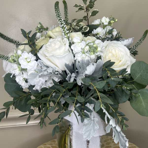 White roses and small white blooms in a glass vase with greenery