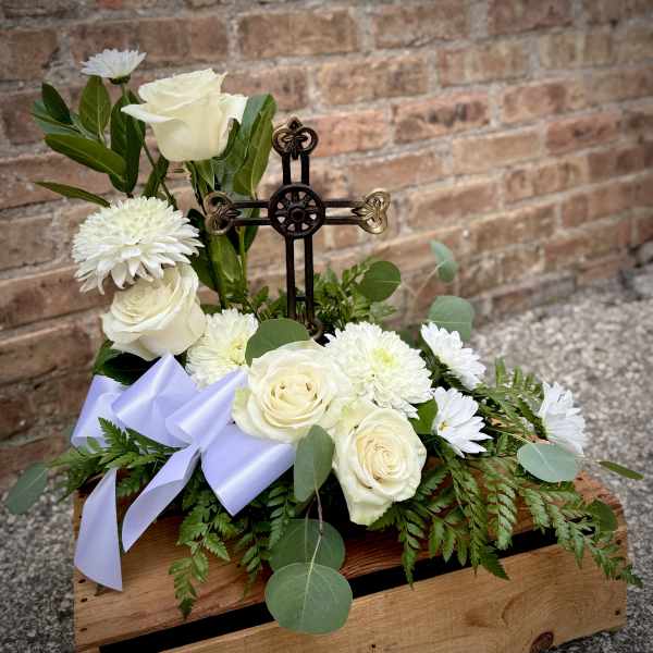 White roses and daisies arranged around a decorative cross in a wooden box