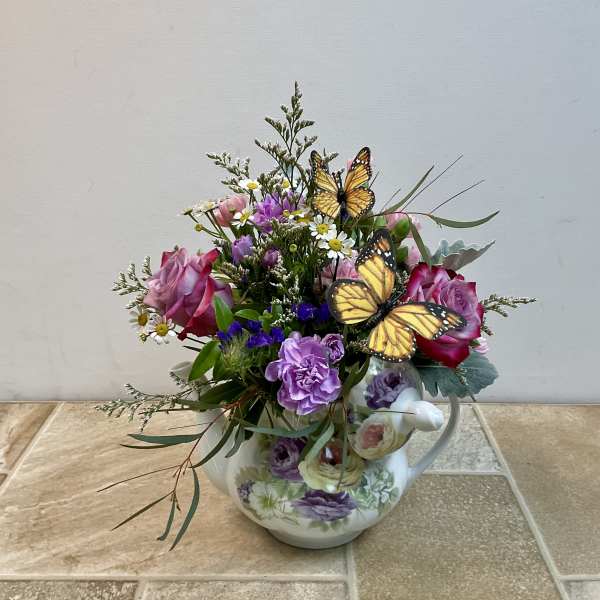 Pink and purple flowers arranged in a floral teapot with butterfly picks