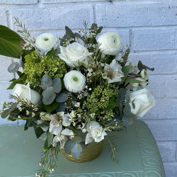White roses and ranunculus in a gold vase with green accents