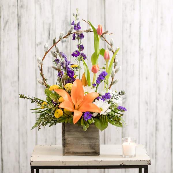 Orange lily bouquet with purple and white flowers in a wooden box