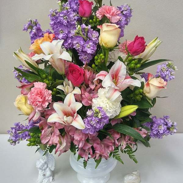 Mixed bouquet of roses, lilies, carnations, and purple flowers in a white vase