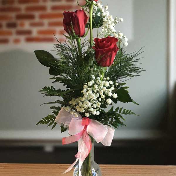 Tall vase arrangement with red roses, baby's breath, and a pink ribbon