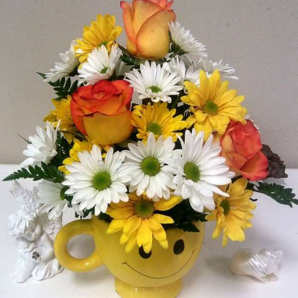 Yellow smiley-face mug filled with daisies and orange roses