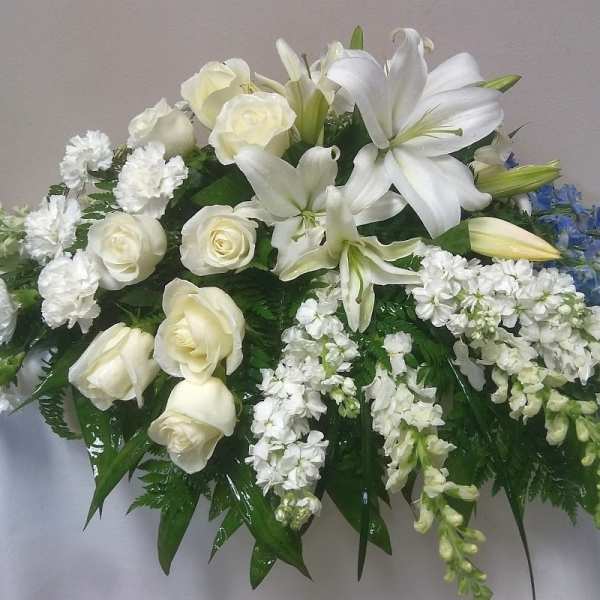 White lilies and roses arranged with blue flowers on a table.