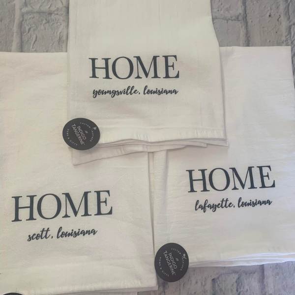 Stacked white towels printed with "HOME" and Louisiana town names