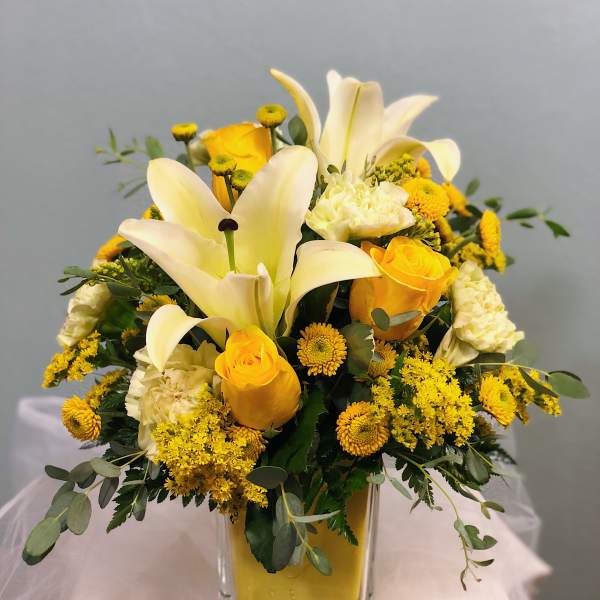 Yellow and white floral arrangement in a clear square vase