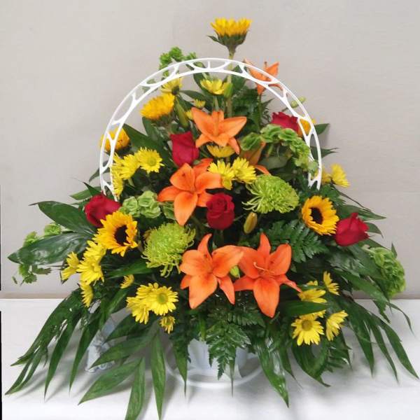Mixed bouquet with orange lilies, red roses, and yellow daisies in a white basket