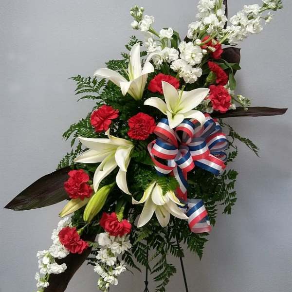 Standing floral spray with white lilies, red carnations, and a patriotic ribbon