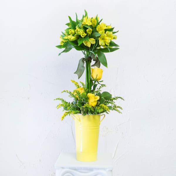 Yellow floral arrangement in a tall yellow container with a ribbon