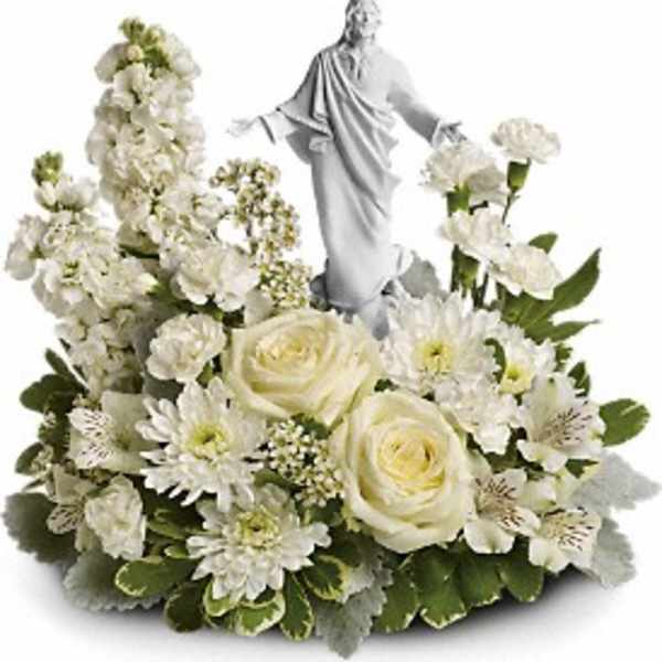 White floral arrangement with roses, carnations, and a central white robed figurine.