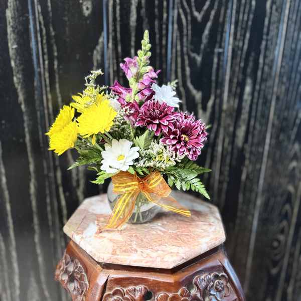 Small mixed flower bouquet in a clear glass vase with an orange ribbon
