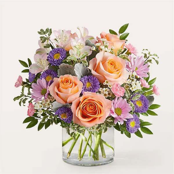 Peach roses and purple daisies in a clear glass vase