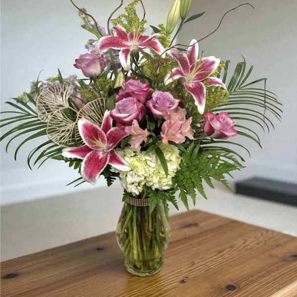 Pink lilies and roses in a glass vase with greenery