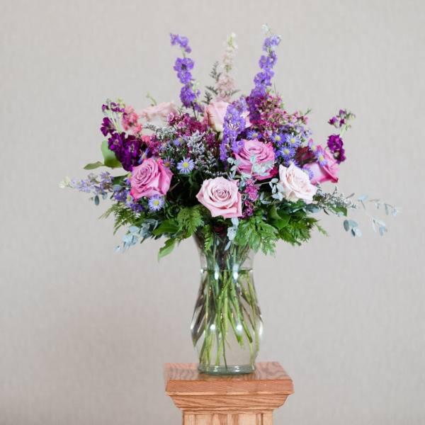 Tall arrangement of pink roses and purple flowers in a clear glass vase