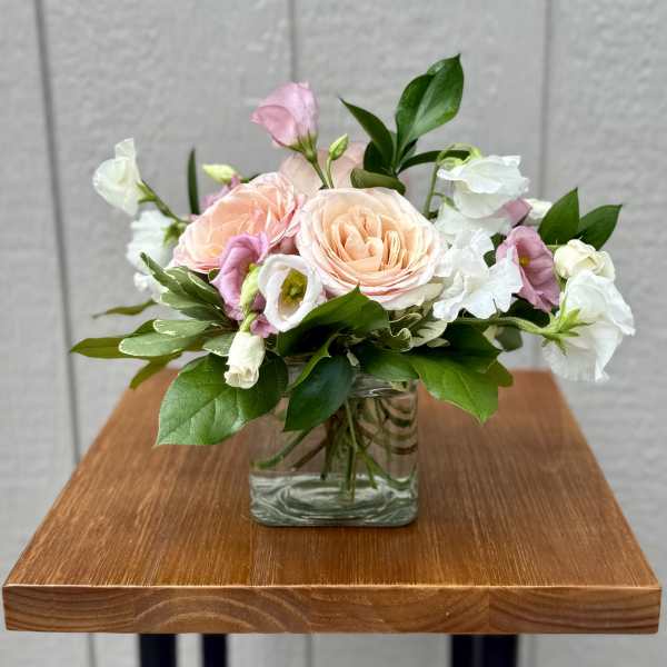 Blush roses and white blooms arranged in a clear glass vase