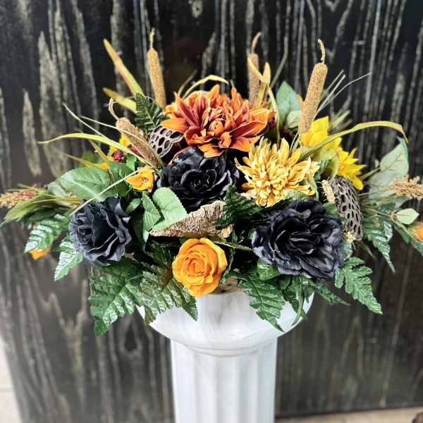 Orange and black floral arrangement in a white pedestal vase