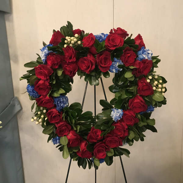 Heart-shaped wreath of red roses with blue flowers on a black stand