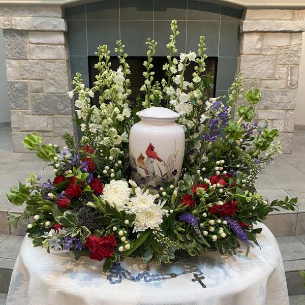 Floral funeral arrangement around a white urn with red, white, and purple flowers