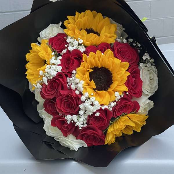 Bouquet of red roses, yellow sunflowers, and white filler flowers in black wrap