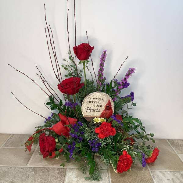 Red roses and purple flowers arranged around a memorial stone.