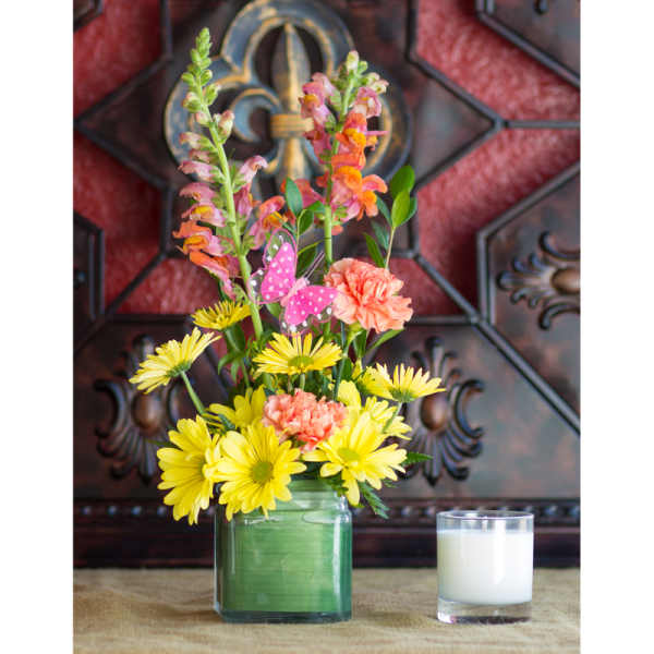 Yellow daisies and pink flowers in a glass vase beside a white candle