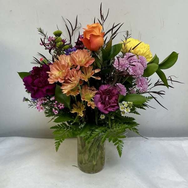 Mixed bouquet in a clear glass vase with orange, yellow, pink, and purple flowers.
