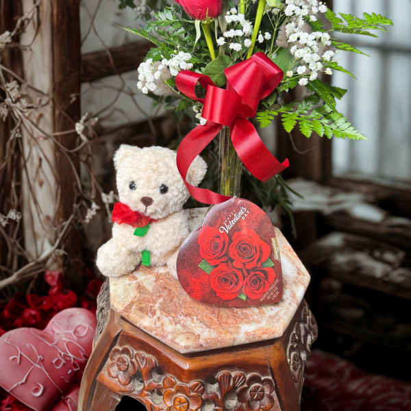 Red roses in a glass vase with a teddy bear and red ribbon