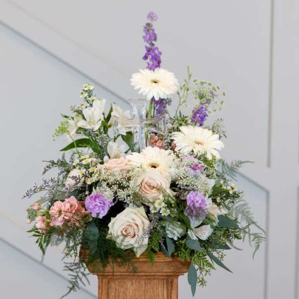 Mixed pastel flower arrangement in a clear glass vase on a wooden pedestal