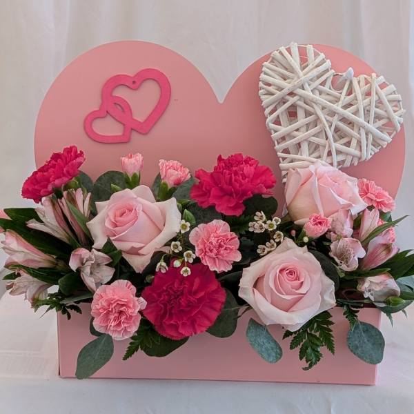 Pink roses and carnations arranged in a heart-shaped box with wicker hearts