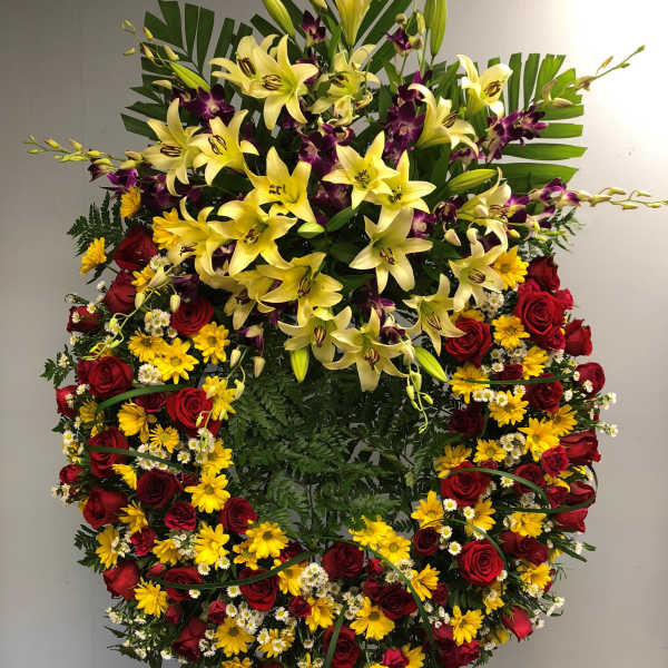 Large standing floral spray with yellow lilies, red roses, and purple orchids