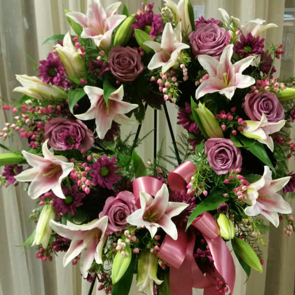 Heart-shaped floral wreath with pink lilies and roses on a stand