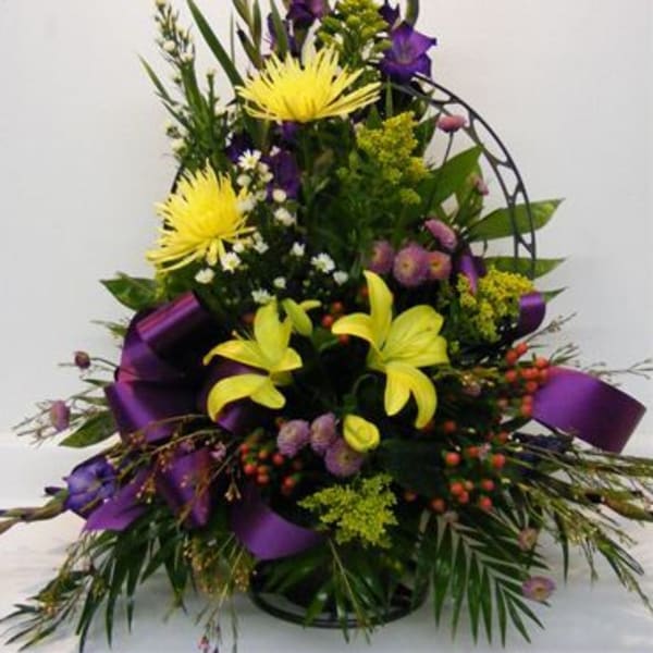 Tall floral arrangement with yellow lilies and purple flowers in a black basket
