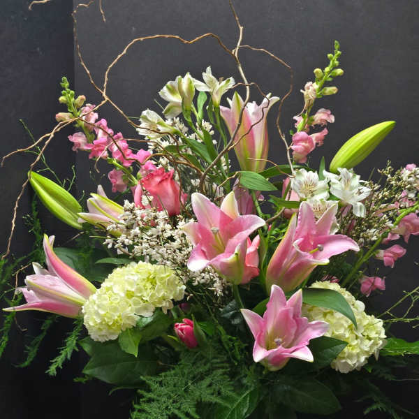 Pink lilies and mixed blooms arranged with curly branches in a vase