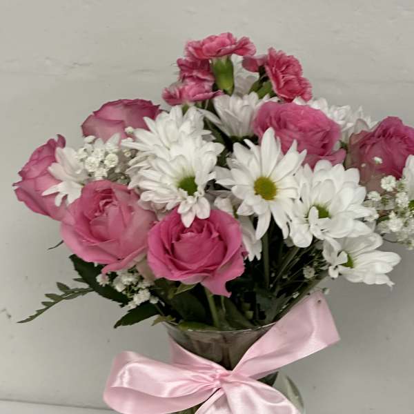 Pink roses and white daisies in a clear vase with a pink ribbon
