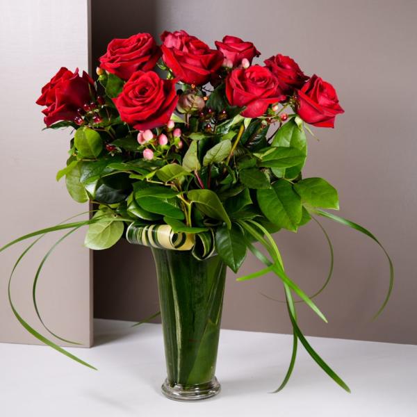 Red roses arranged in a tall glass vase with greenery