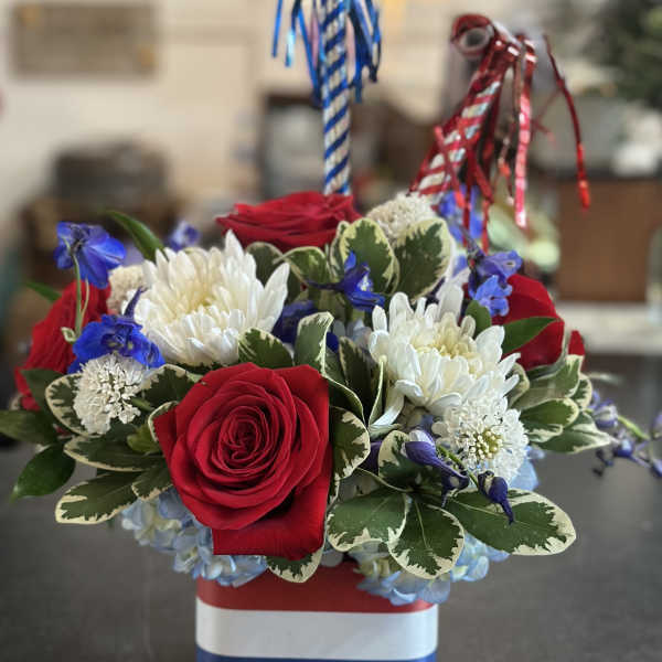 Red roses and white chrysanthemums in a patriotic striped container with blue and red ribbons