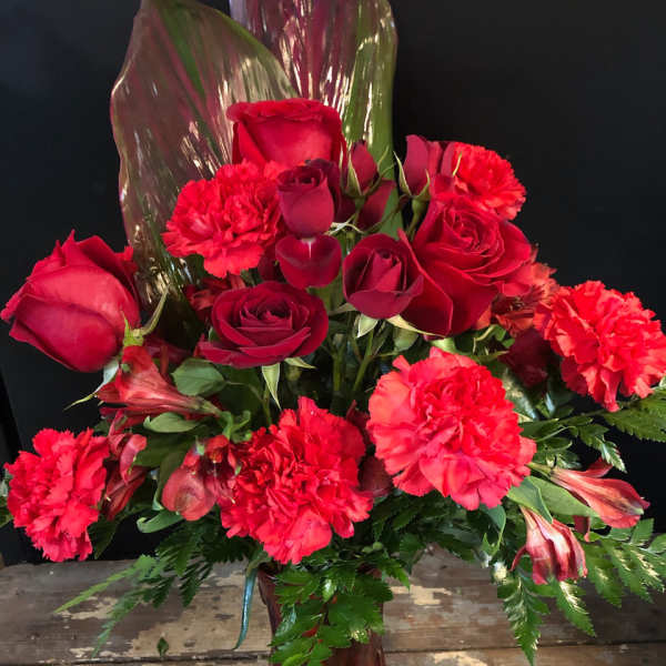 Red roses and carnations arranged in a vase with tropical leaves