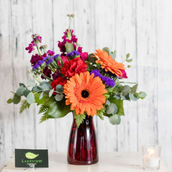 Orange gerbera daisies and mixed flowers in a red vase