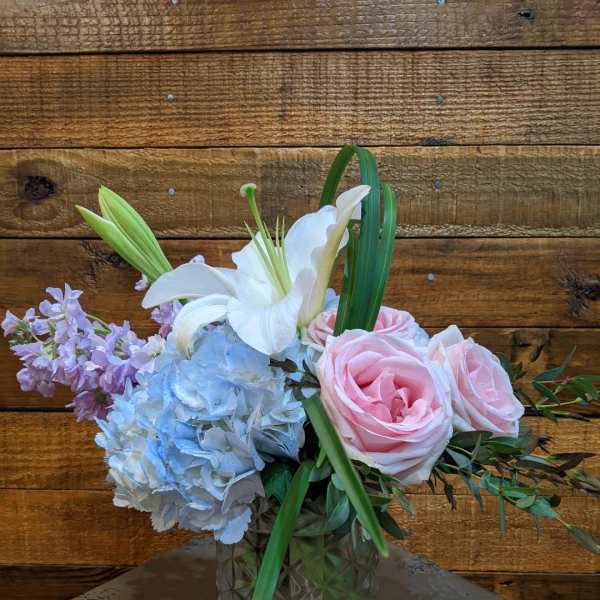 Pink roses, blue hydrangea, and a white lily in a glass vase