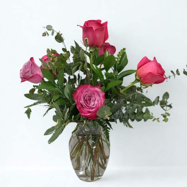 Pink roses arranged in a clear glass vase with greenery