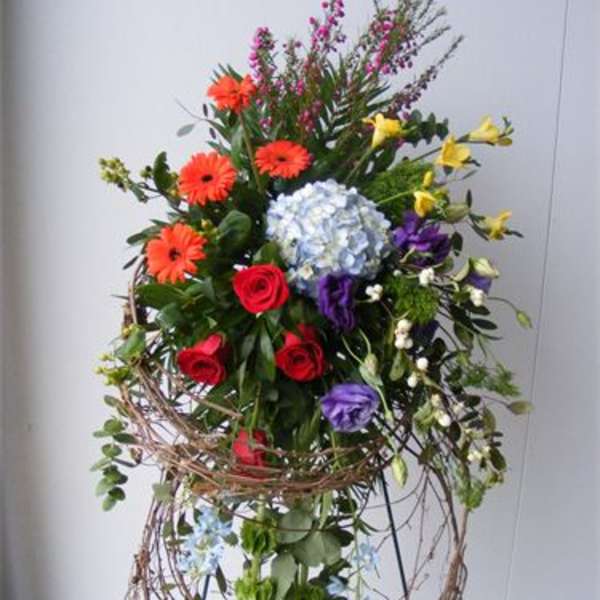 Tall mixed flower arrangement with roses, gerberas, and hydrangea in a wire stand